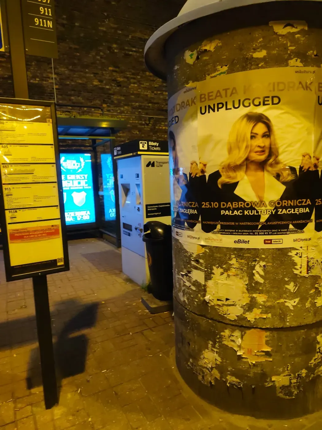 Plakat koncertu Beata Kozidrak Unplugged na słupie obok przystanku, rozkładu jazdy i biletomatu
