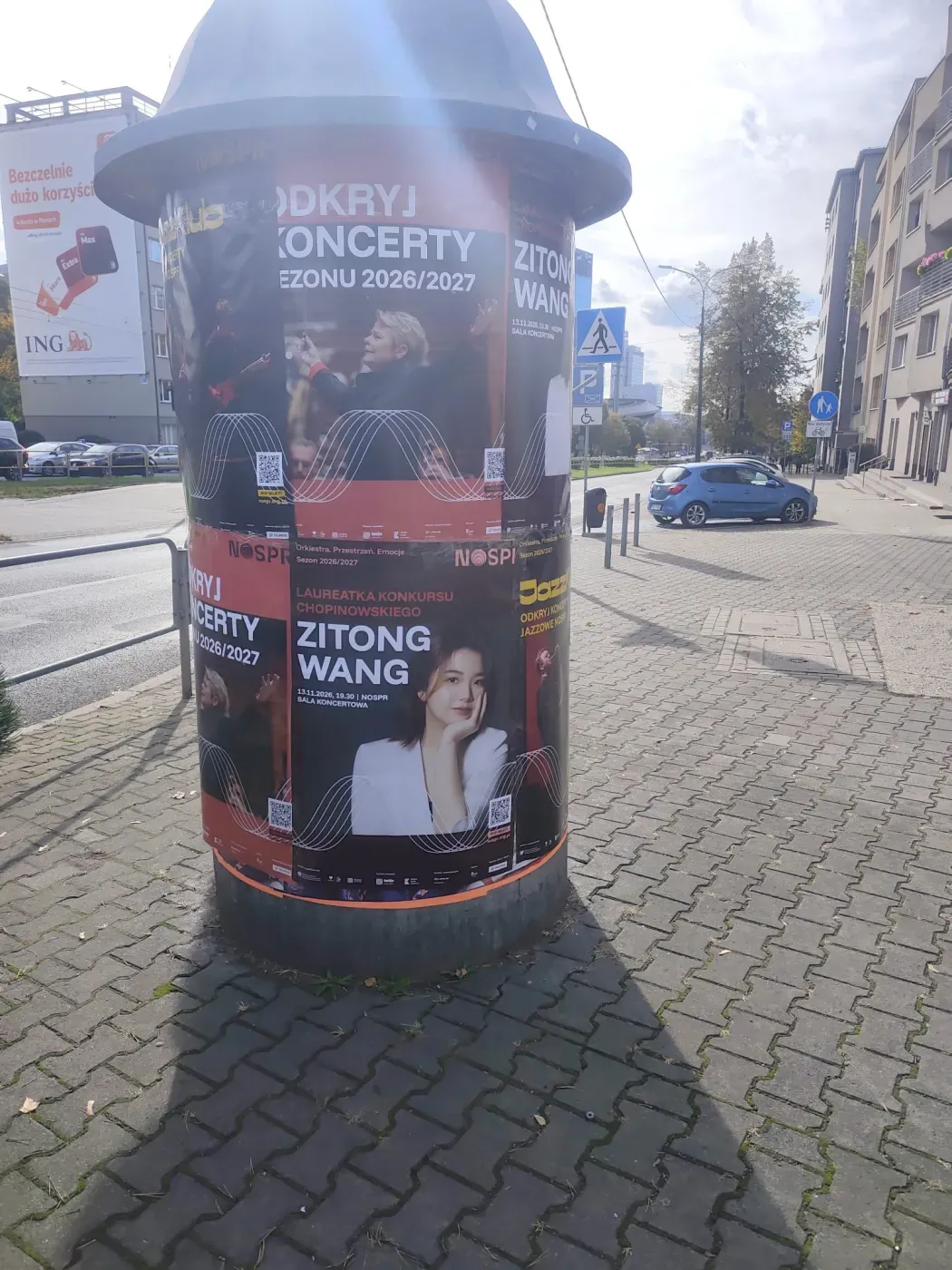 Plakaty koncertu Zitong Wang na słupie przy ruchliwej ulicy w Katowicach