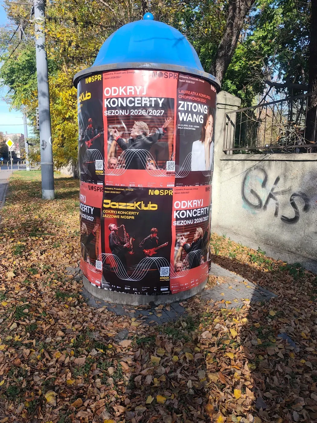 Słup ogłoszeniowy z plakatami sezonu koncertowego i JazzKlubu wśród jesiennych liści