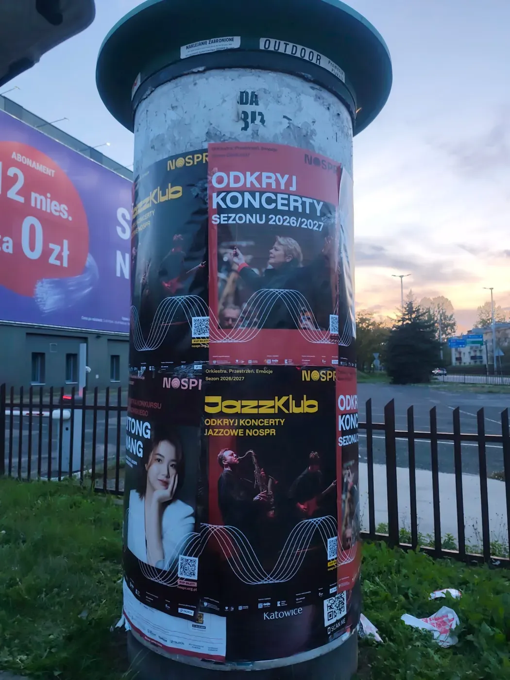 Słup ogłoszeniowy z plakatami koncertowymi przy ulicy i ogrodzeniu w Katowicach