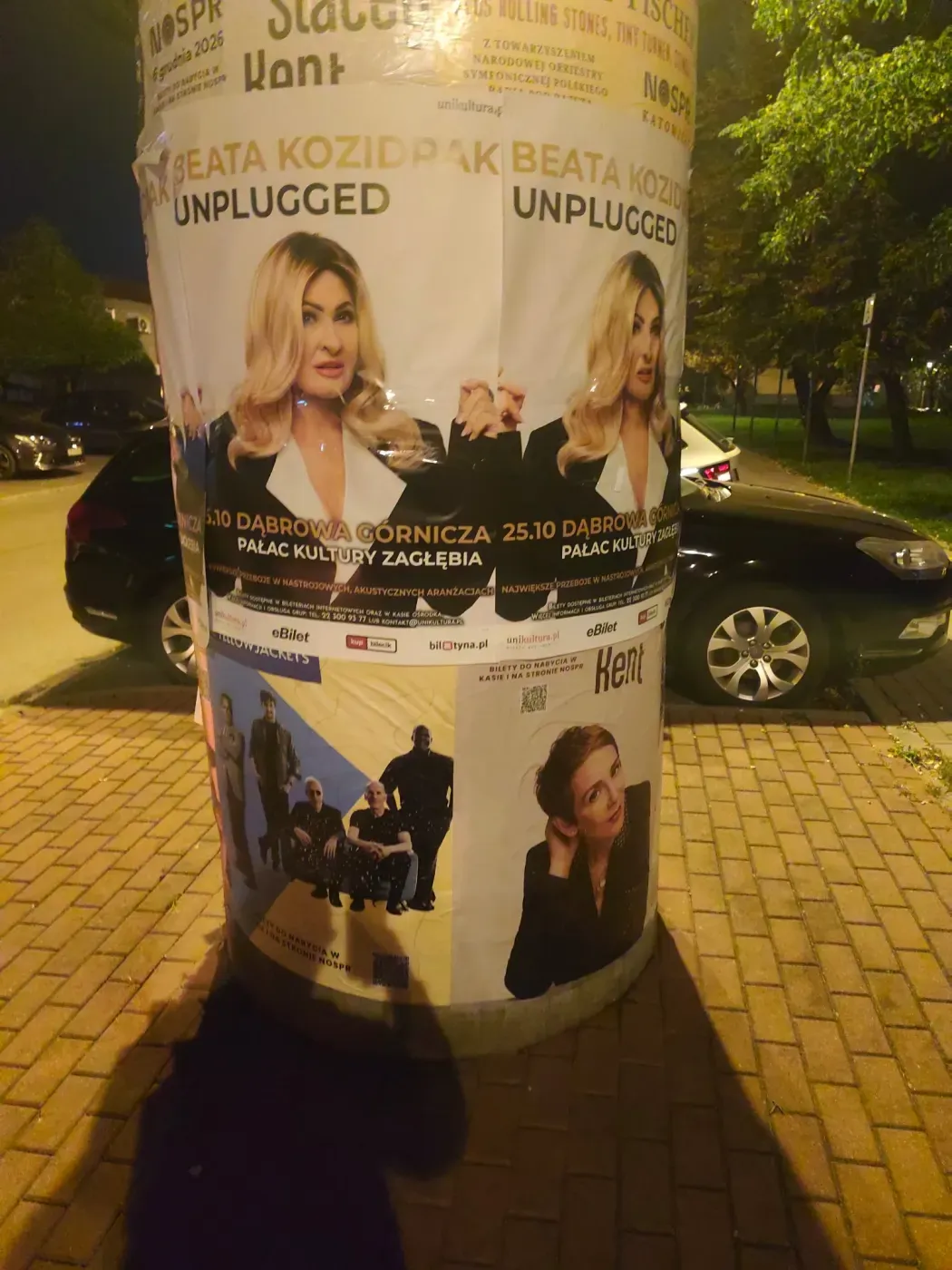 Plakat koncertu Beata Kozidrak Unplugged na słupie przy zaparkowanych samochodach