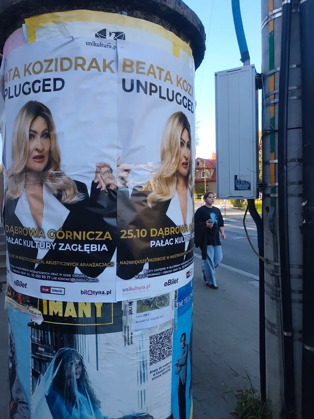 Plakaty Beata Kozidrak Unplugged na słupie przy chodniku, obok przechodzi piesza