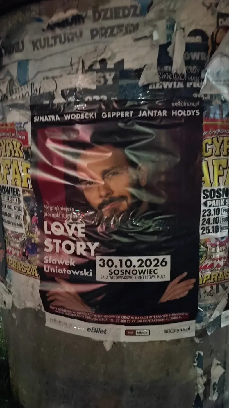 Plakat koncertu Love Story na słupie ogłoszeniowym między innymi afiszami.