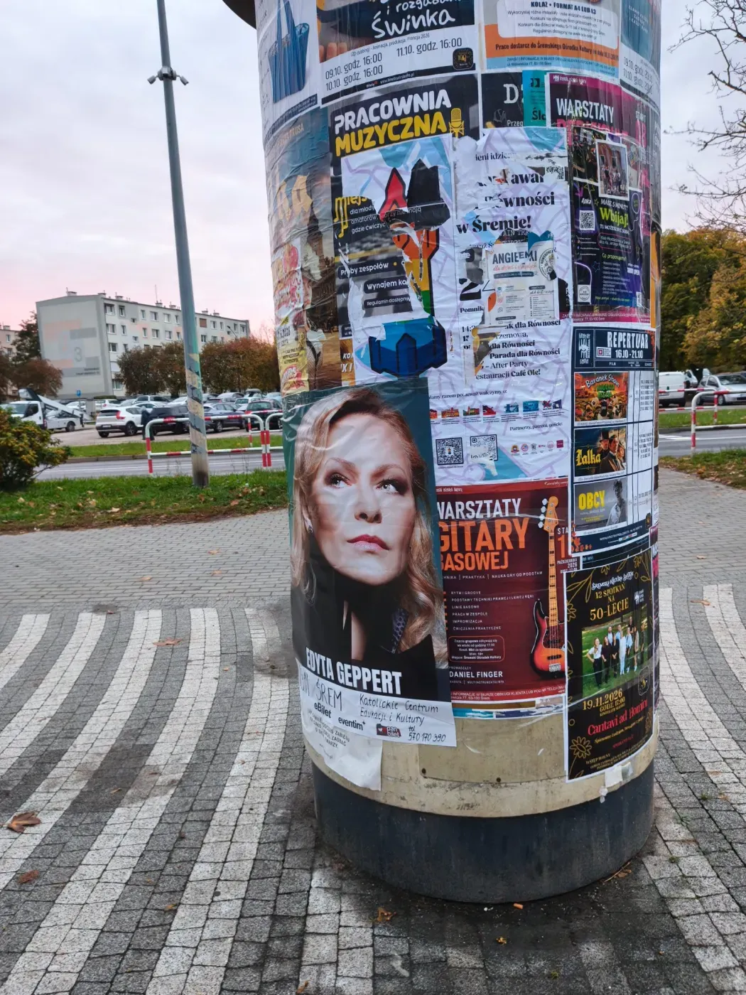 Plakat Edyty Geppert na słupie ogłoszeniowym przy chodniku i parkingu w Śremie