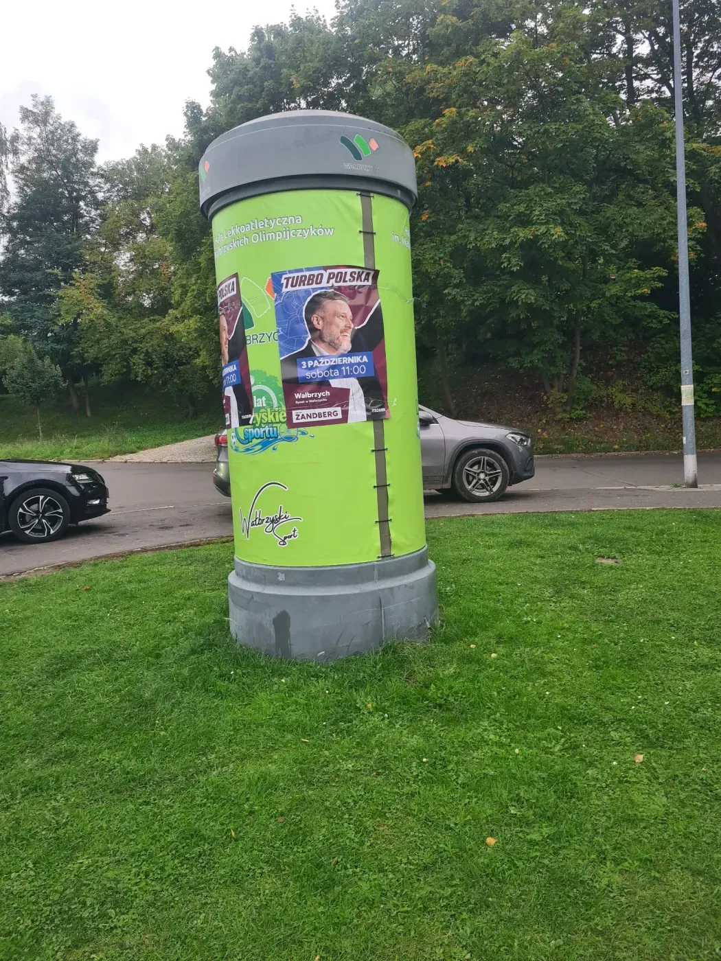 Plakat Turbo Polska na zielonym słupie ogłoszeniowym przy ulicy i terenie zielonym w Wałbrzychu