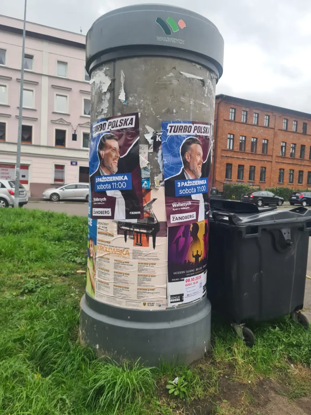 Dwa plakaty Turbo Polska na słupie ogłoszeniowym obok pojemników i zabudowy w Wałbrzychu